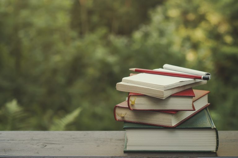 pile of books on a garden wooden table, green nature background